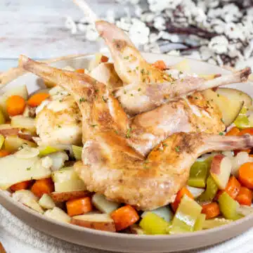Wide image of a whole roasted rabbit with root vegetables.