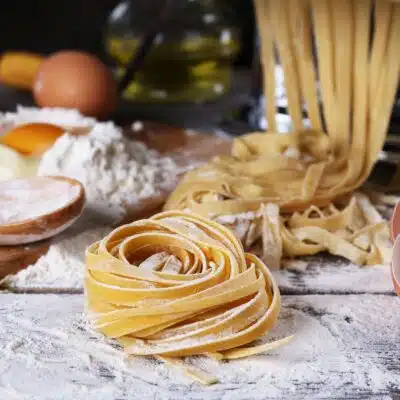 Square image of homemade pasta with pasta making supplies.