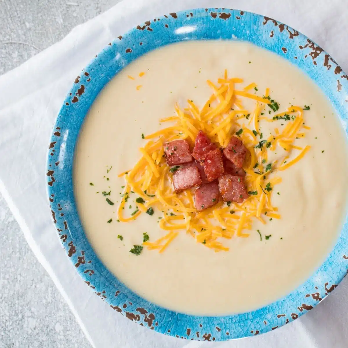 Square image of creamy cauliflower soup in a blue bowl.