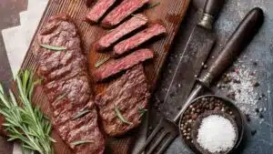 Wide image of sliced Denver steak on a cutting board.