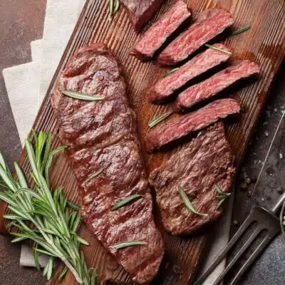 Square image of sliced Denver steak on a cutting board.