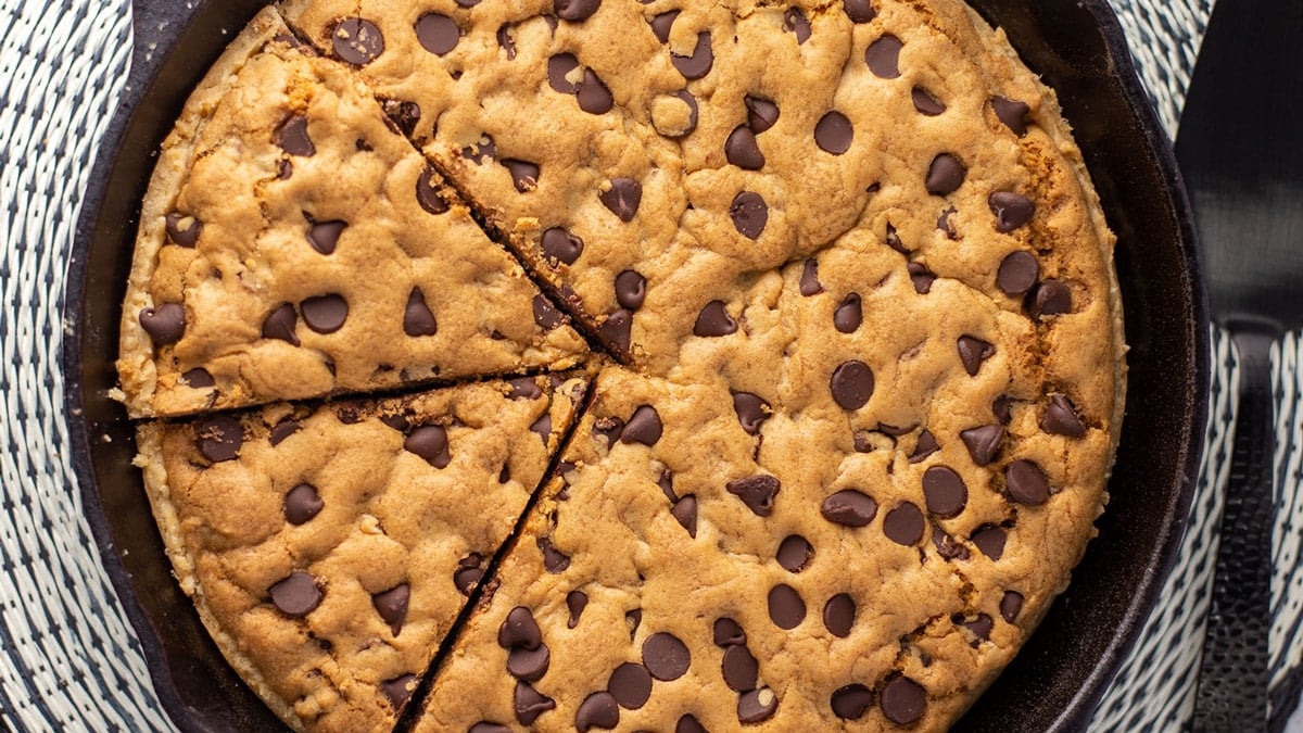 Friskbagt chocolate chip cookie pie i en støbejernsgryde med to skiver skåret.