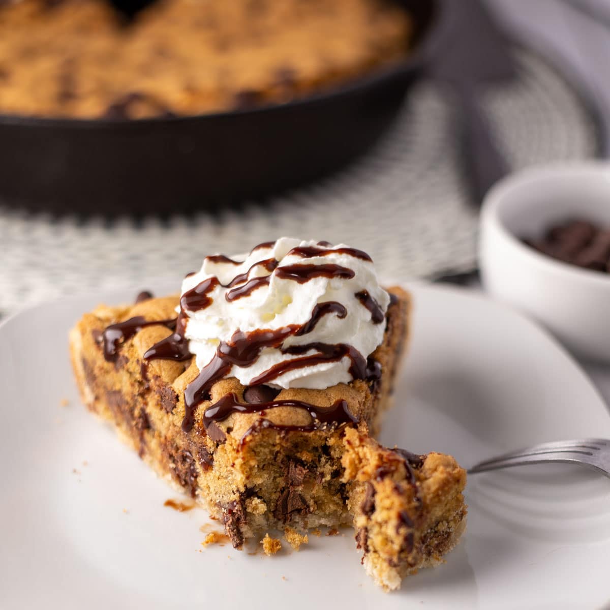 Mør, velsmagende chocolate chip cookie pie skåret i skiver og serveret med flødeskum og chokoladesauce.