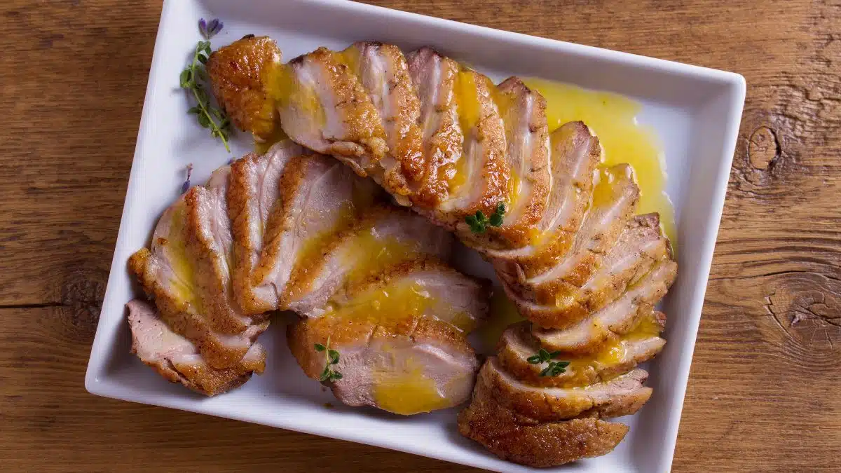 Wide image of sliced duck with orange sauce.