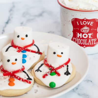 Square image showing melting snowman sugar cookies with some hot cocoa.