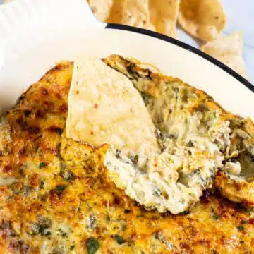 Wide image of baked hot spinach and artichoke dip with chips.