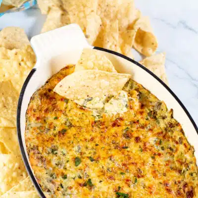 Square image of baked hot spinach and artichoke dip with chips.