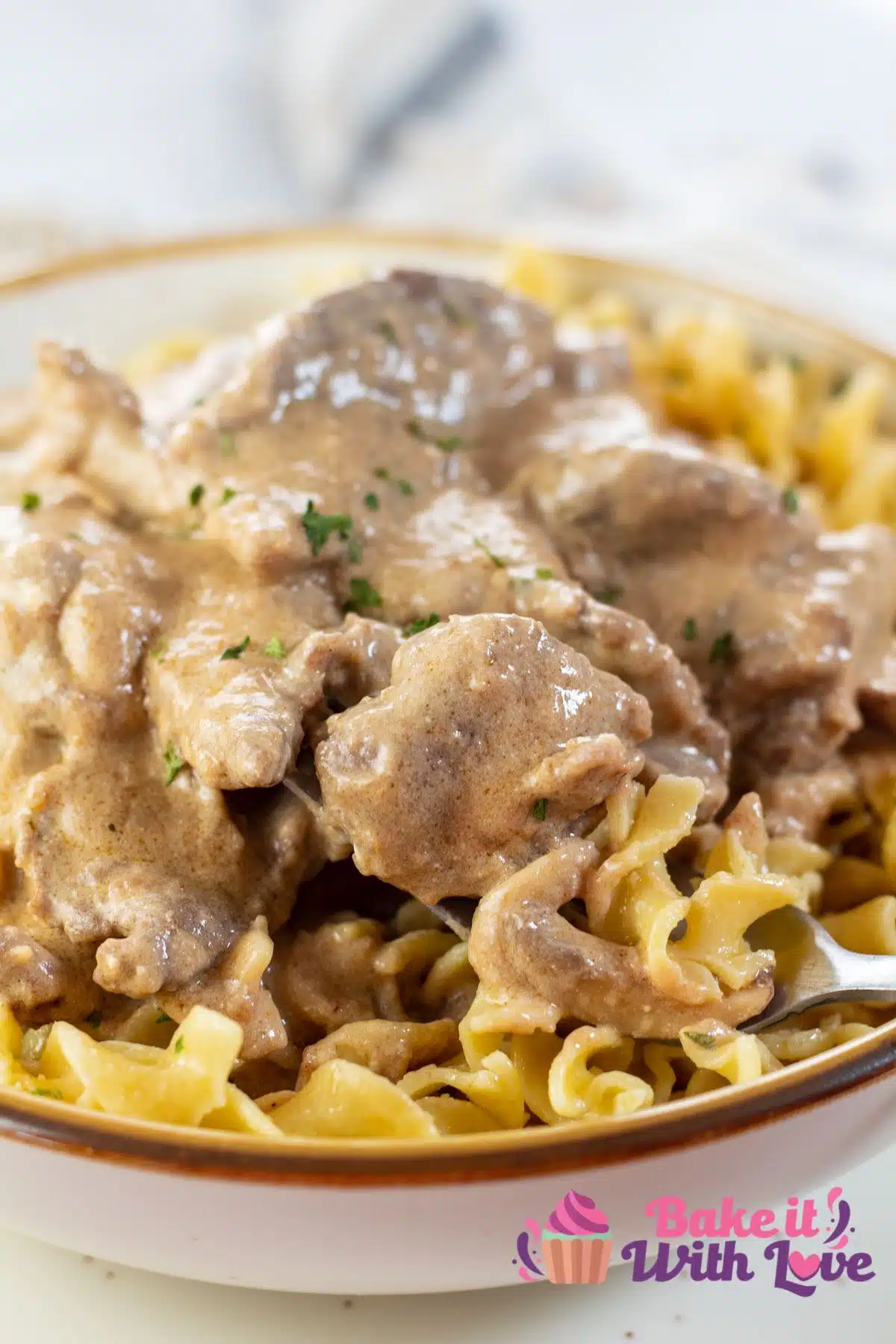 Tall image of beef stroganoff over buttered egg noodles.