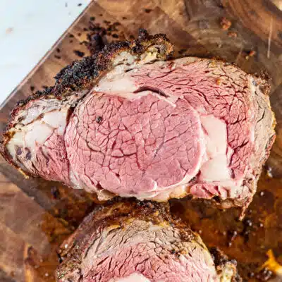 Tender, delicious, and evenly cooked no peek prime rib roast sliced on wooden grain cutting board.