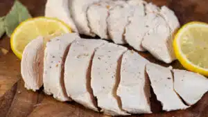 Sliced poached chicken breasts with lemons and bay leaves on a cutting board ready to dish up or chop for casseroles.
