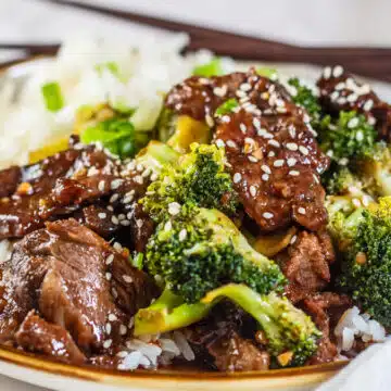 Wide view of the plated prime rib beef broccoli stir fry on a plate with chopsticks in the background.
