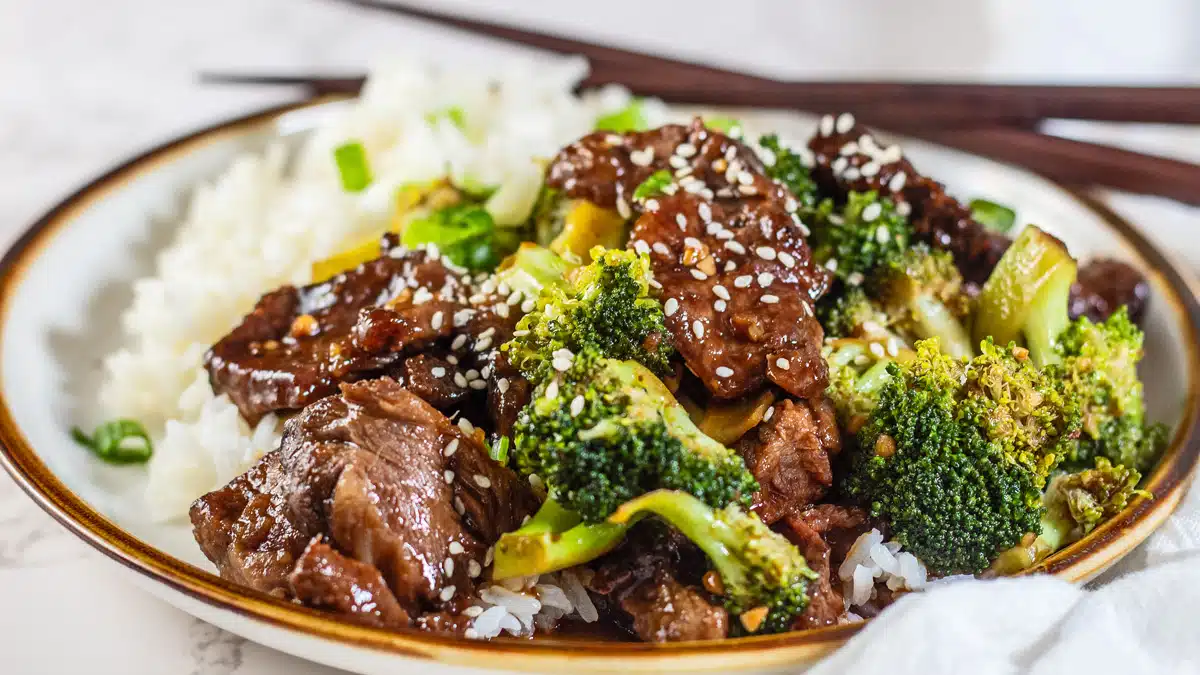 Wide view of the plated prime rib beef broccoli stir fry on a plate with chopsticks in the background.