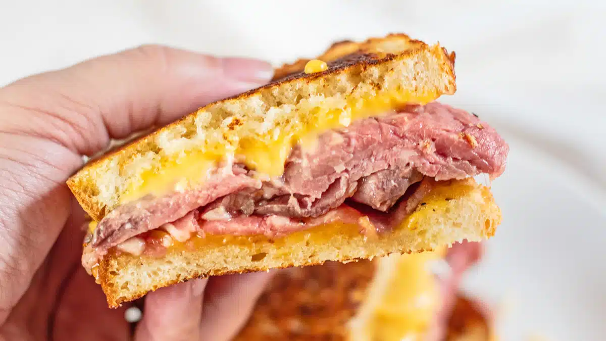 Sliced prime rib grilled cheese sandwich in hand showing the tender sliced beef and melty cheese.