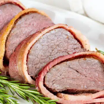 Wide image of bacon wrapped beef tenderloin, sliced.