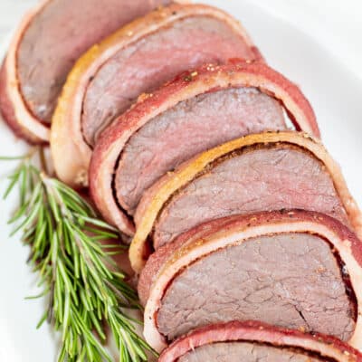 Square image of bacon wrapped beef tenderloin, sliced.