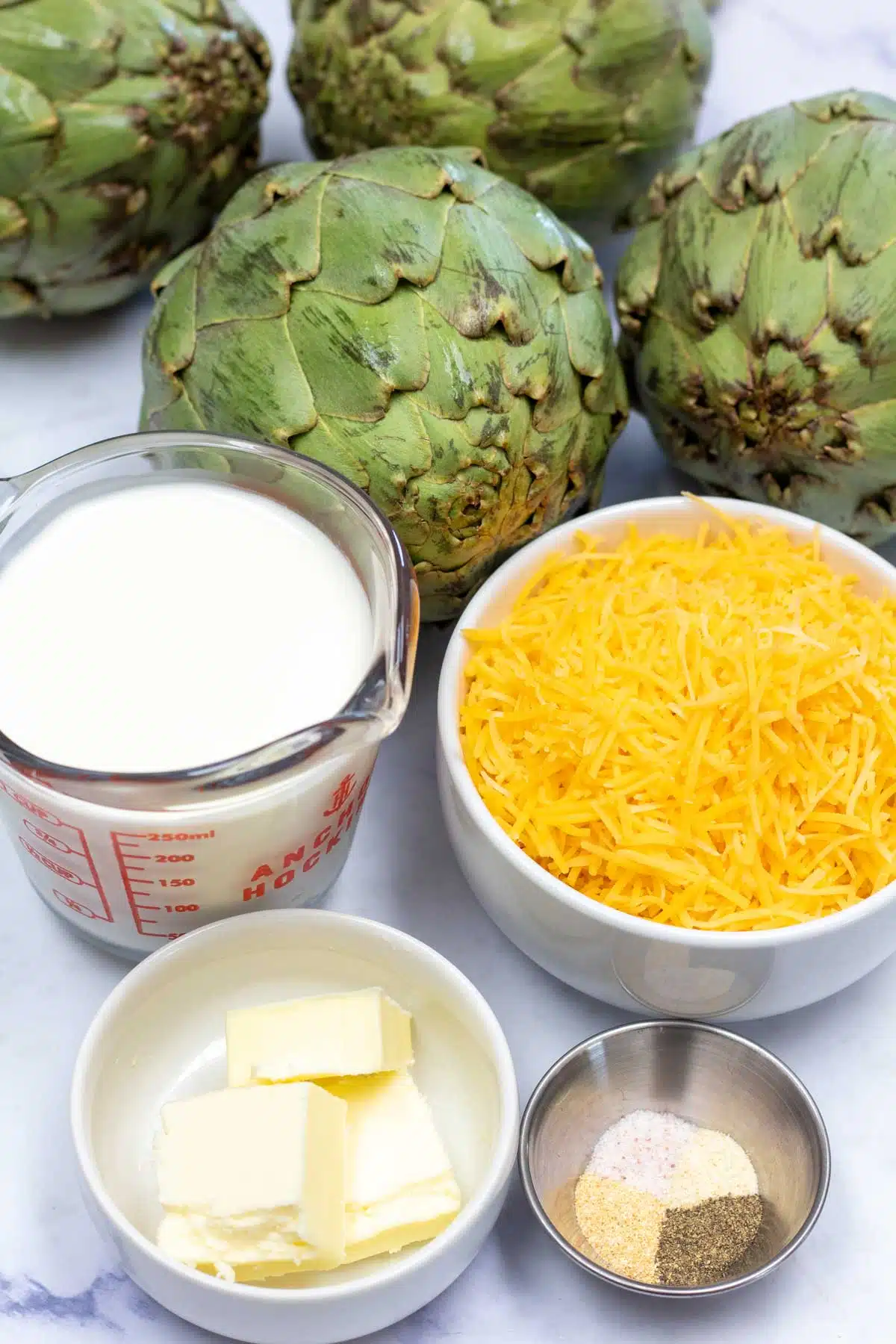 Tall image showing the ingredients needed for steamed artichokes and cheese sauce.
