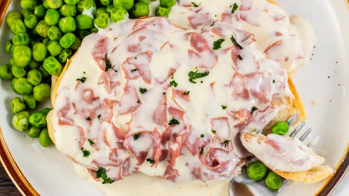 Creamed chipped beef on toast with peas on the side served on tan plate.