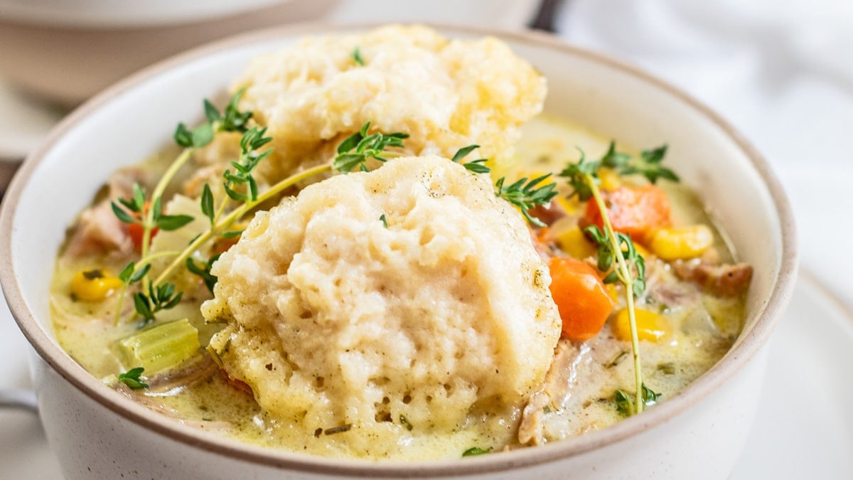 Creamy turkey and dumplings in light beige bowl with fresh thyme as garnish.