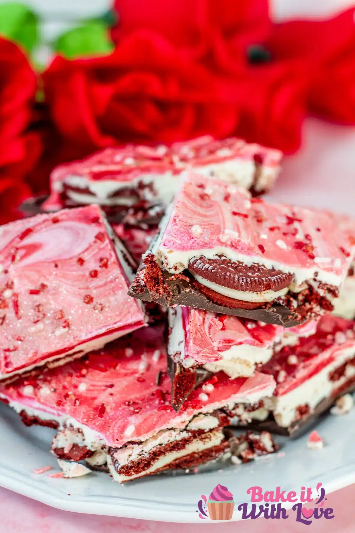 Beautiful red roses in the background of homemade Valentine's Day Oreo chocolate bark stacked on white plate.