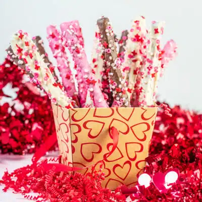 Valentine's Day pretzel rods with chocolate and festive sprinkles standing upright in a valentine's box.