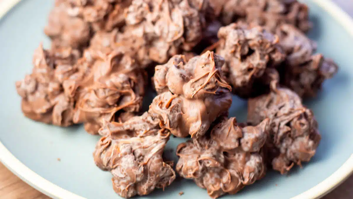 Wide image of chocolate raisin candy clusters on a blue plate.