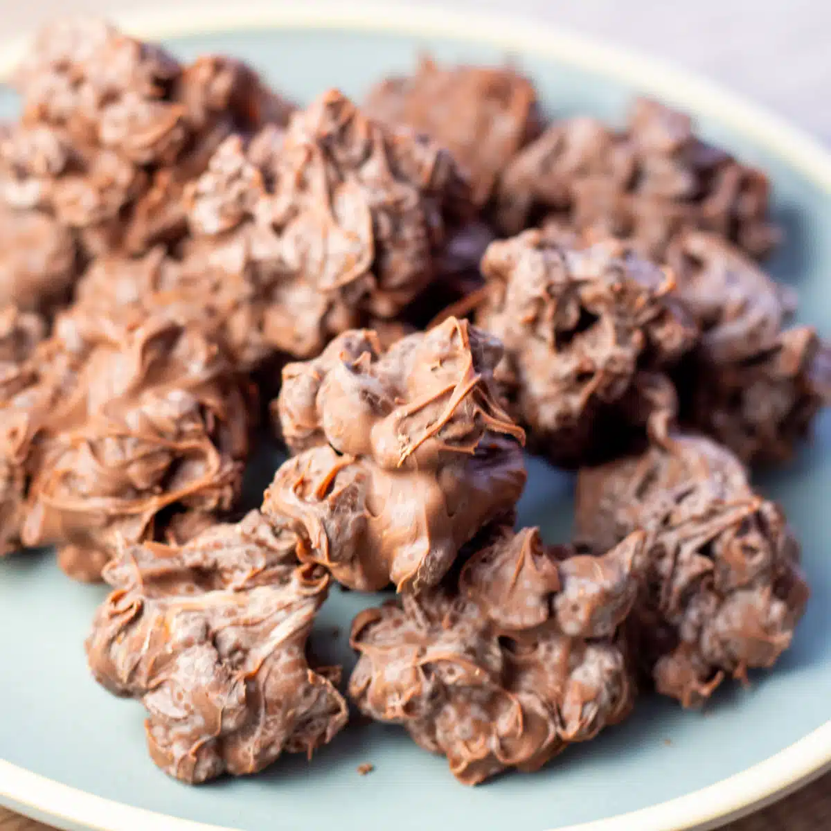 Square image of chocolate raisin candy clusters on a blue plate.