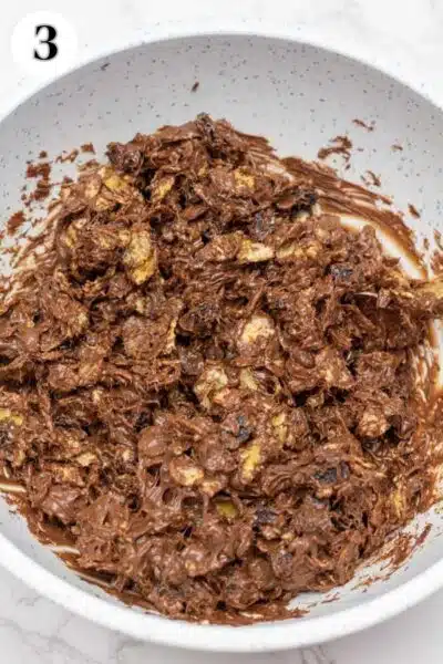 Process image showing melted chocolate with cornflakes and raisins all combined together in mixing bowl.