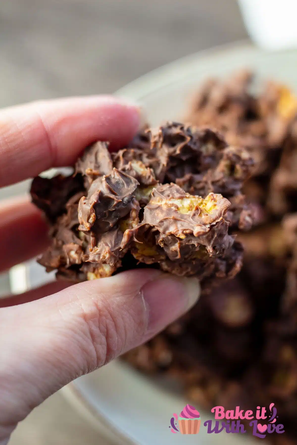 Tall image of chocolate raisin cornflakes candy clusters being held by hand.