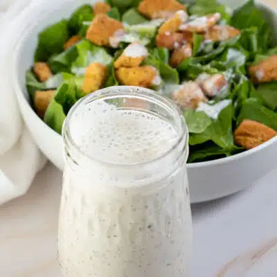 Square image of creamy Italian dressing next to a bowl of salad.