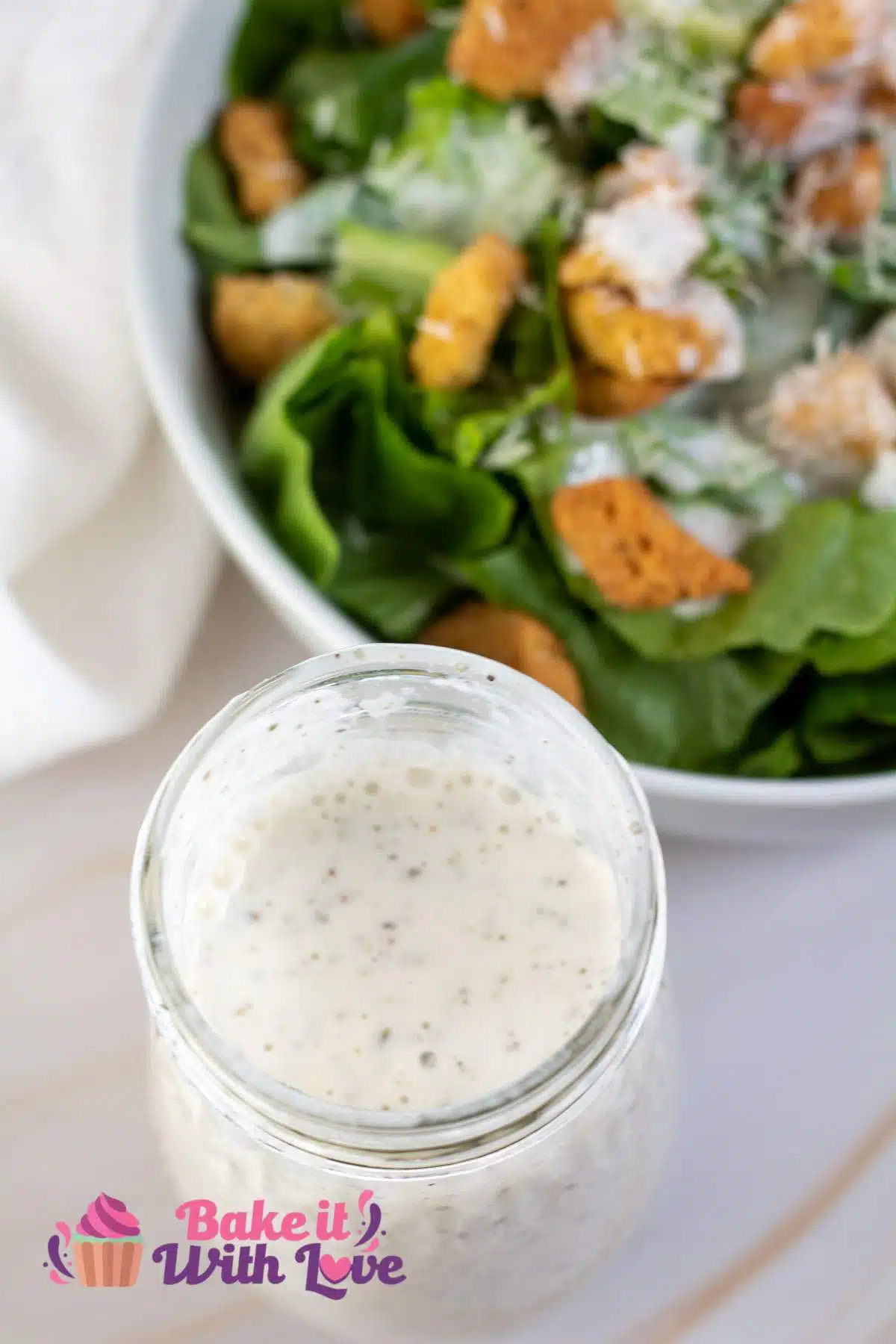 Tall image of creamy Italian dressing next to a bowl of salad.