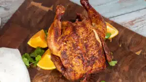 Wide image of smoked beer can chicken on a cutting board.
