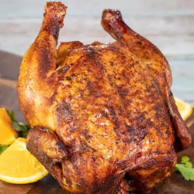 Squaree image of smoked beer can chicken on a cutting board.