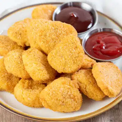 Square image of air fried chicken nuggets on a plate with ketchup and BBQ sauce.