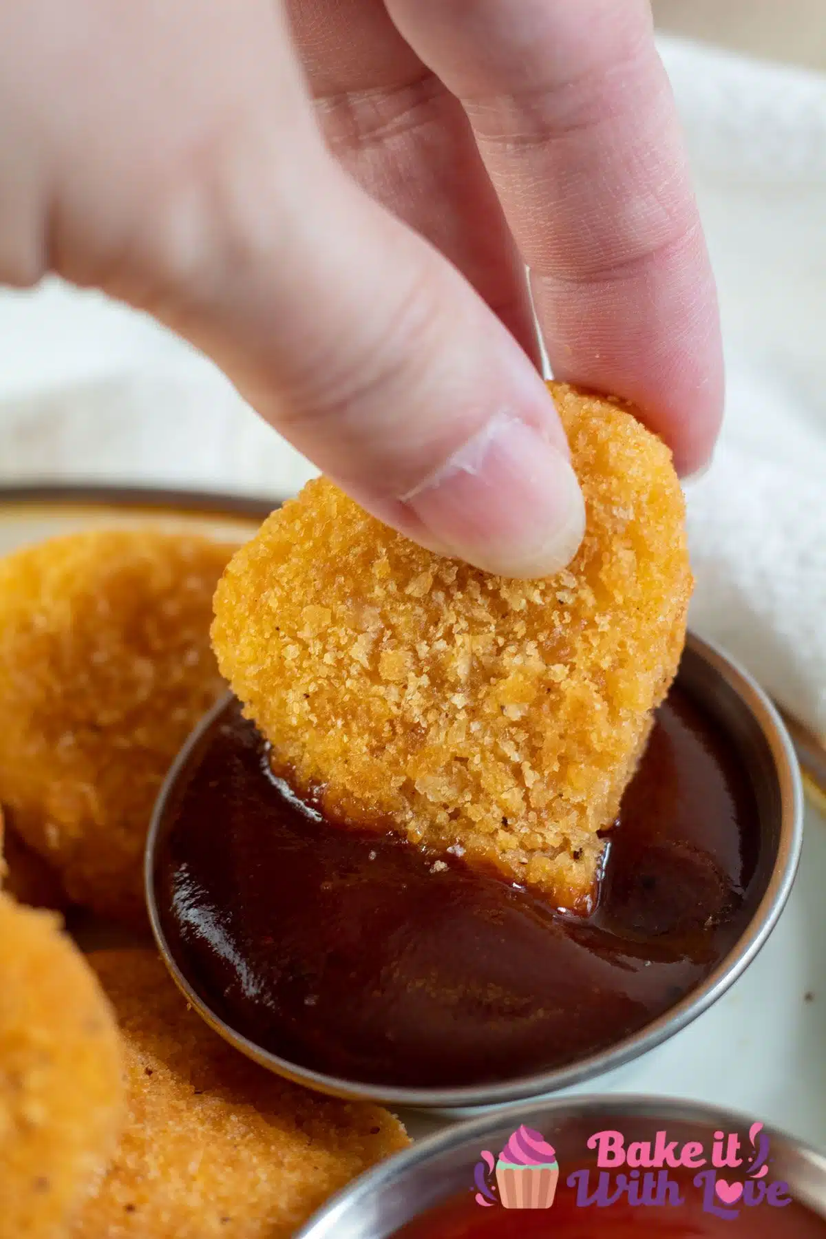 Tall image of air fried chicken nugget being dipped in BBQ sauce.