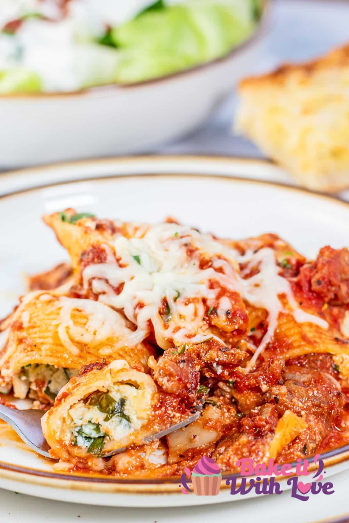 Flavorful, hearty baked stuffed shells plated with salad and crusty French bread in the background.
