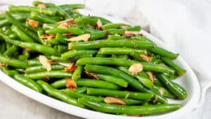 Wide image of a white serving plate with green beans almondine.