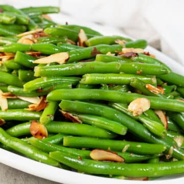 Wide image of a white serving plate with green beans almondine.