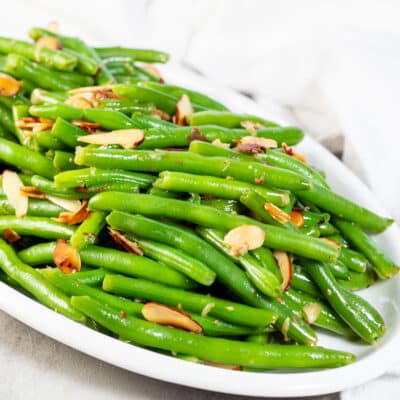 Square image of a white serving plate with green beans almondine.