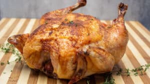 Wide image of roast Capon chicken on a cutting board.