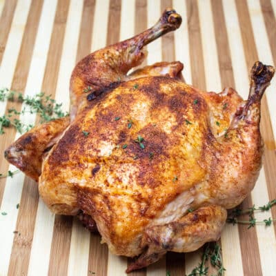 Firkantet billede af stegt Capon kylling på et skærebræt.