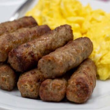 Wide image of air fried sausage links cooked from frozen on a plate with scrambled eggs.