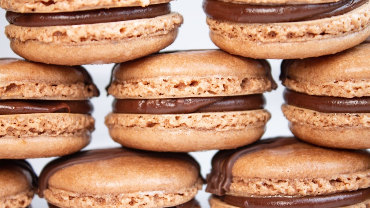 Wide closeup image of stacked chocolate macarons on light background.