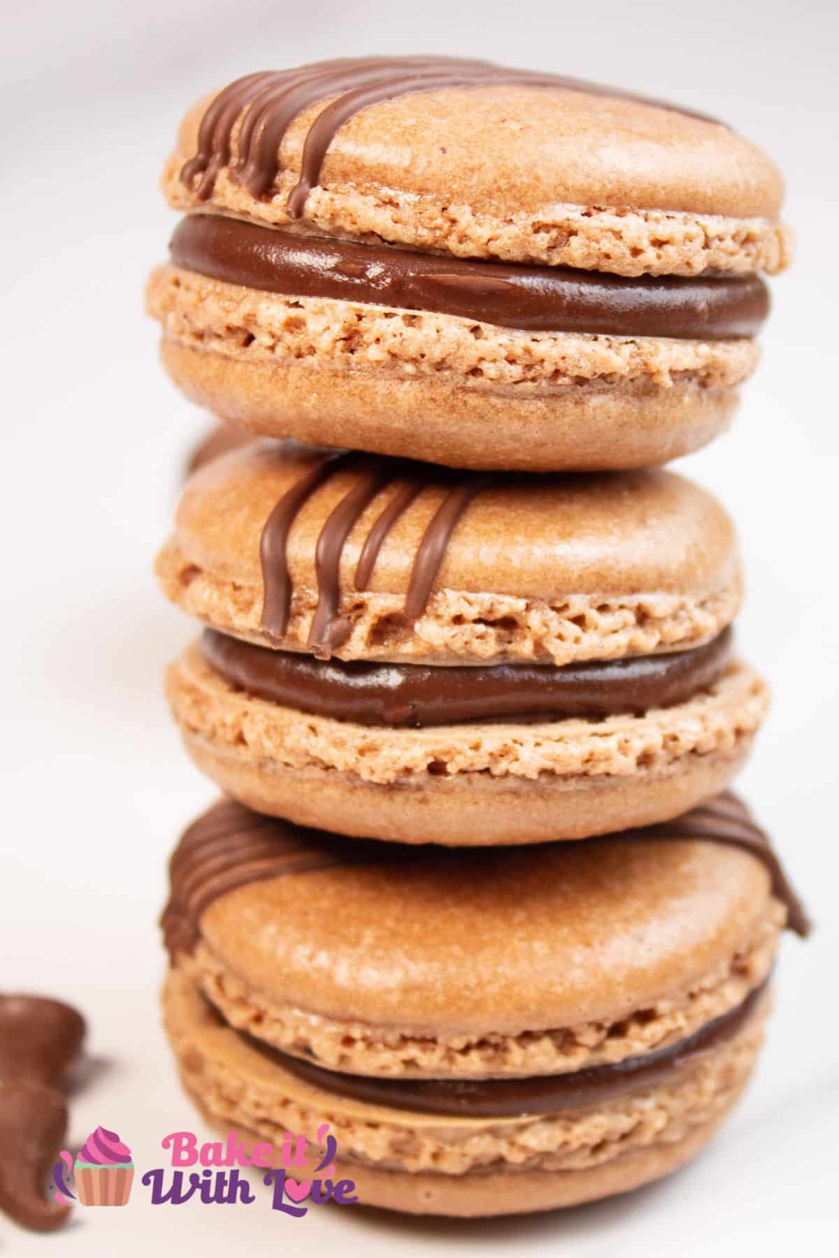 Tall stack of the chocolate macarons on light background with a few chocolate morsels scattered at the base.