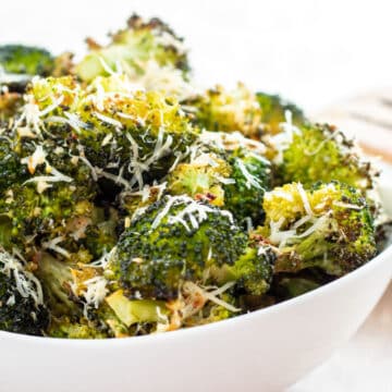 Wide image of roasted broccoli with garlic and Parmesan cheese in a white bowl.