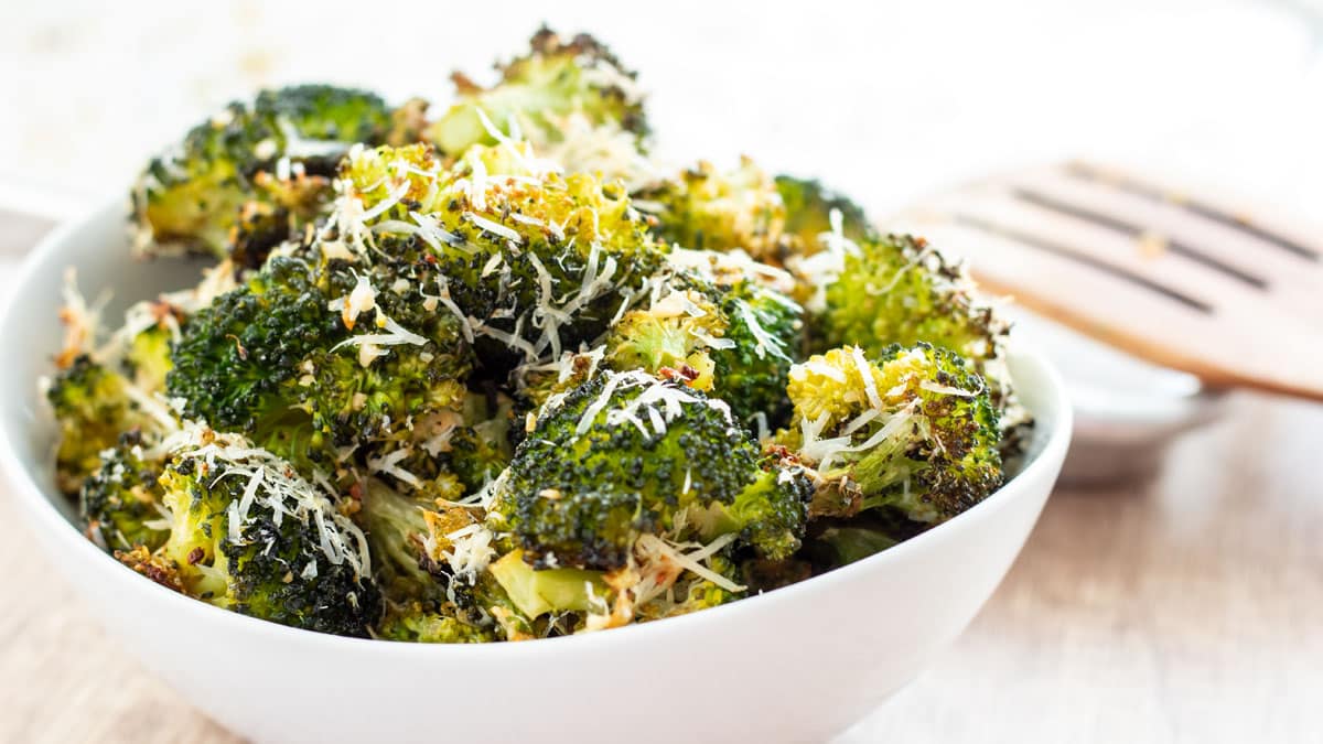 Wide image of roasted broccoli with garlic and Parmesan cheese in a white bowl.