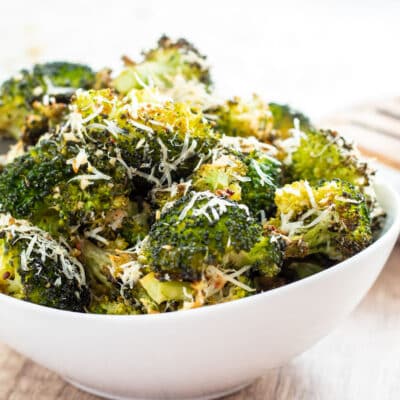 Square image of roasted broccoli with garlic and Parmesan cheese in a white bowl.