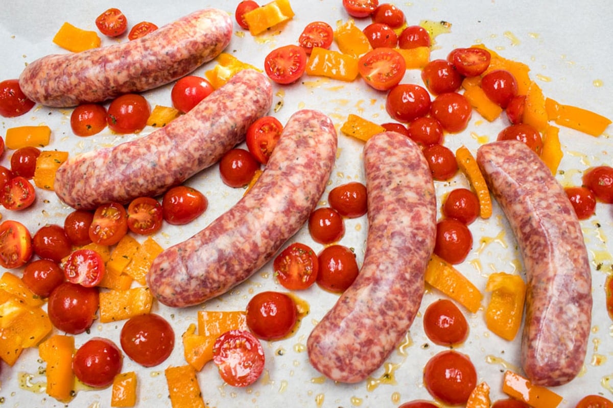 Process phot of preparing baked Italian sausages on a parchment paper lined baking sheet.