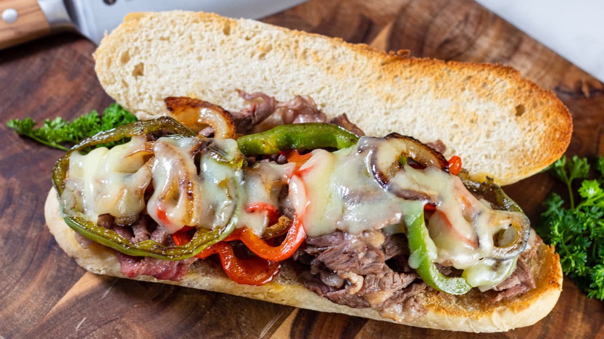 Wide image of open Philly cheese-steak sandwich on a cutting board.