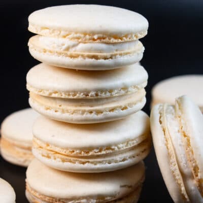 Best vanilla macaron recipe with stacked macarons on black background.