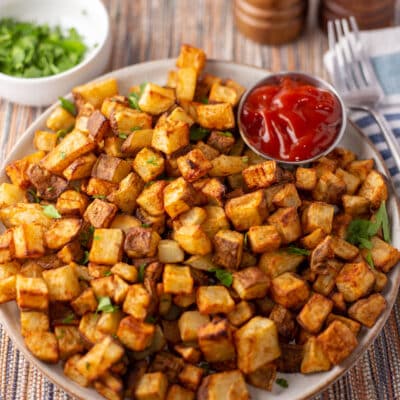 Tasty homemade air fryer home fries served with a small bowl of ketchup and garnished with parsley.